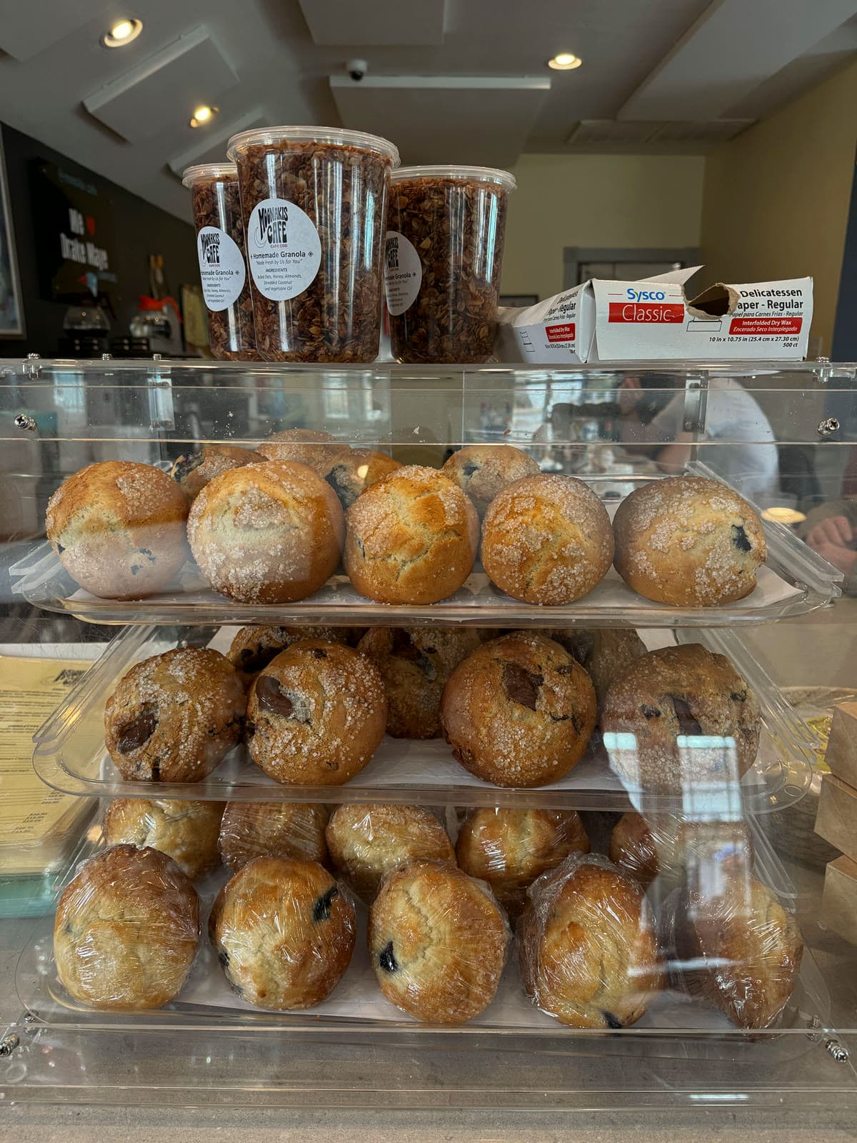 Bakery case with trays of sugar-topped muffins and labeled jars of homemade granola on top