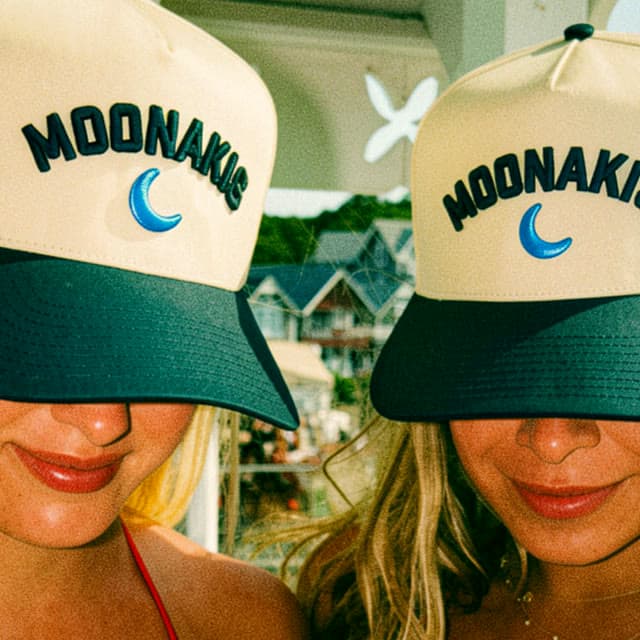 Two people wearing cream and navy Moonakis ball caps with an embroidered blue crescent moon