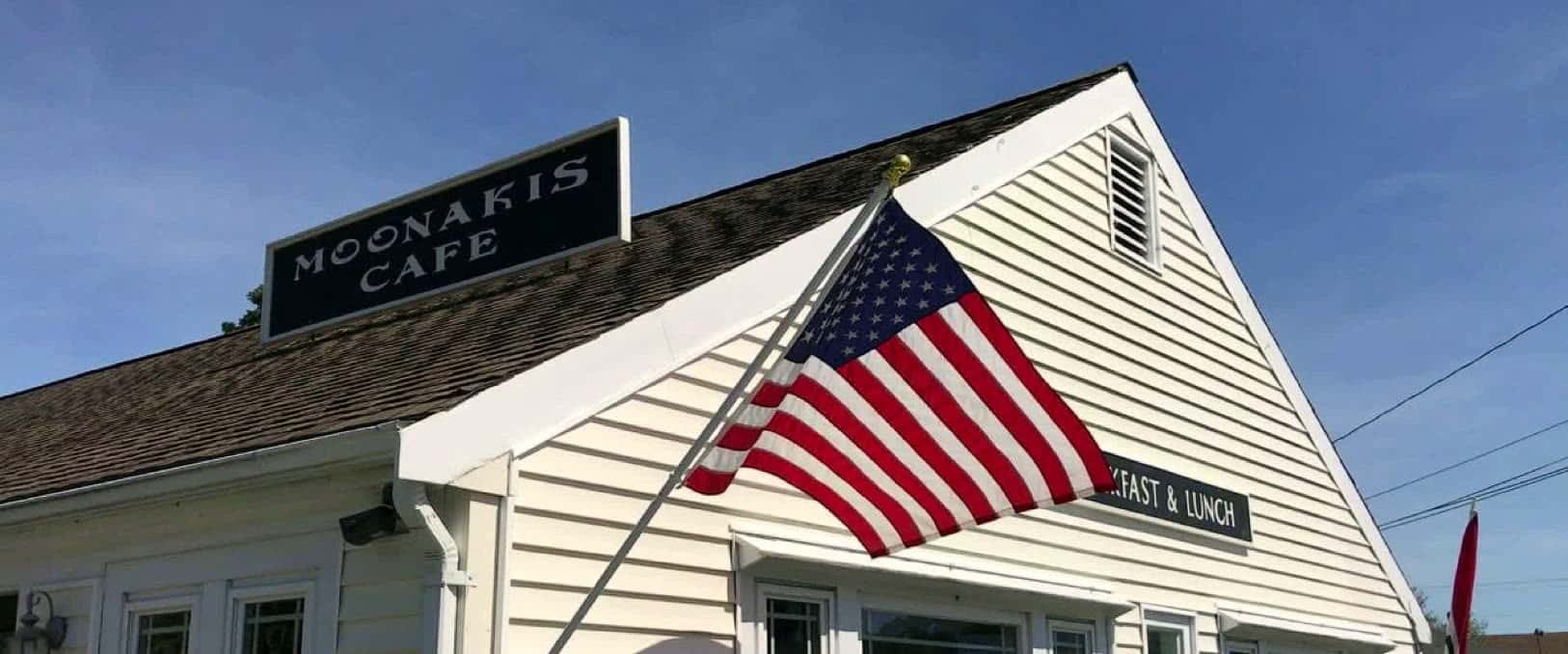 The white gable of Moonakis Cafe with its rooftop sign and an American flag against a blue sky