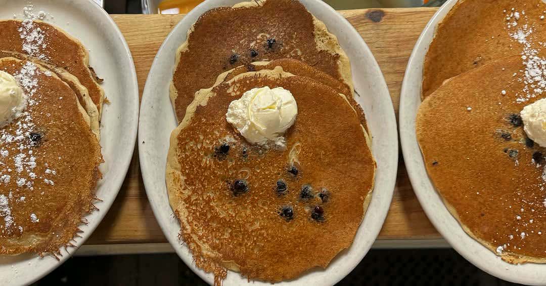 Plates of blueberry pancakes with whipped butter on the counter at Moonakis Cafe