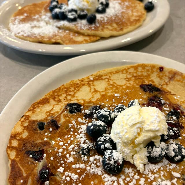 Blueberry pancakes off the griddle with a melting dollop on top and powdered sugar