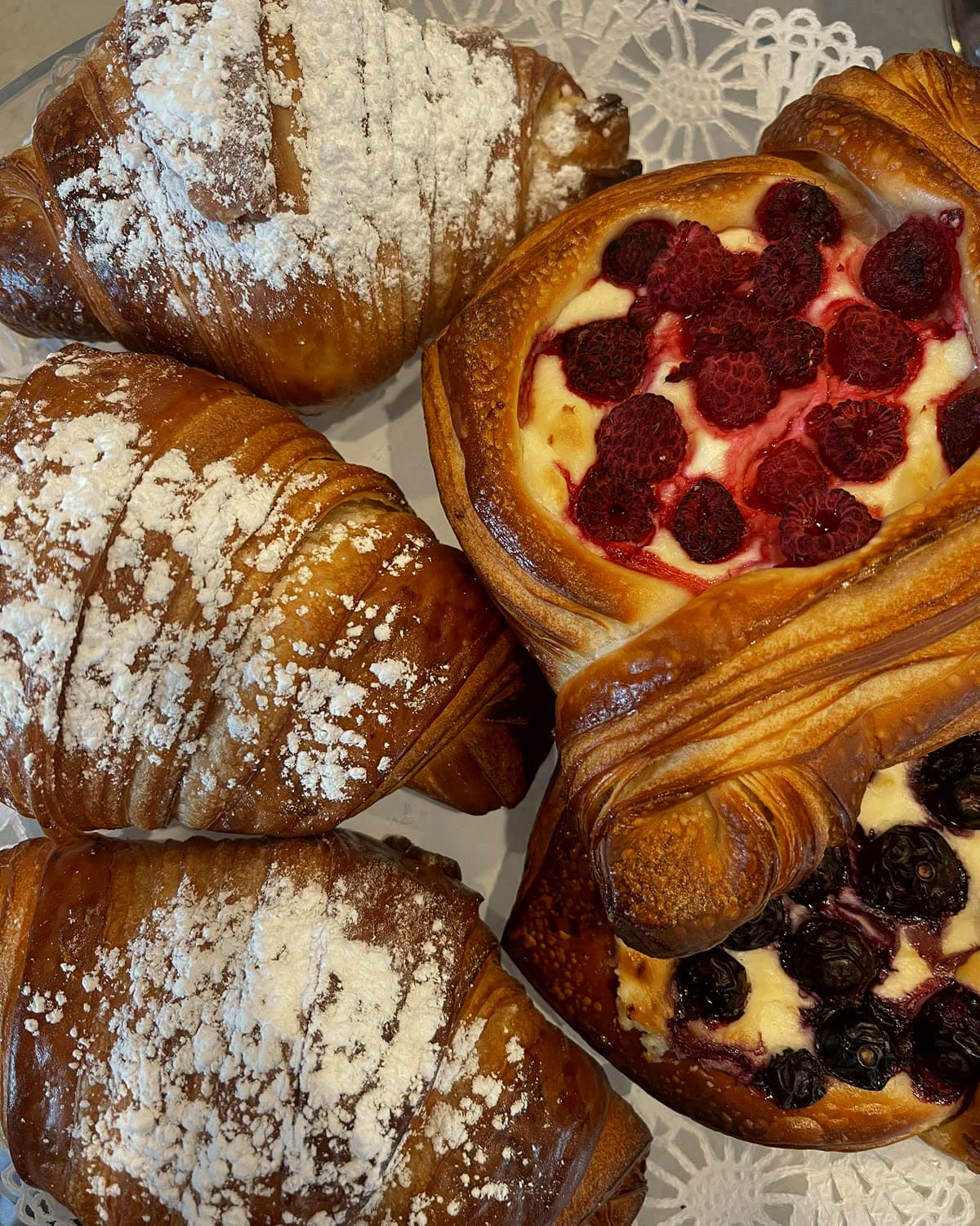 Croissants dusted with powdered sugar beside raspberry and blueberry cream cheese danishes