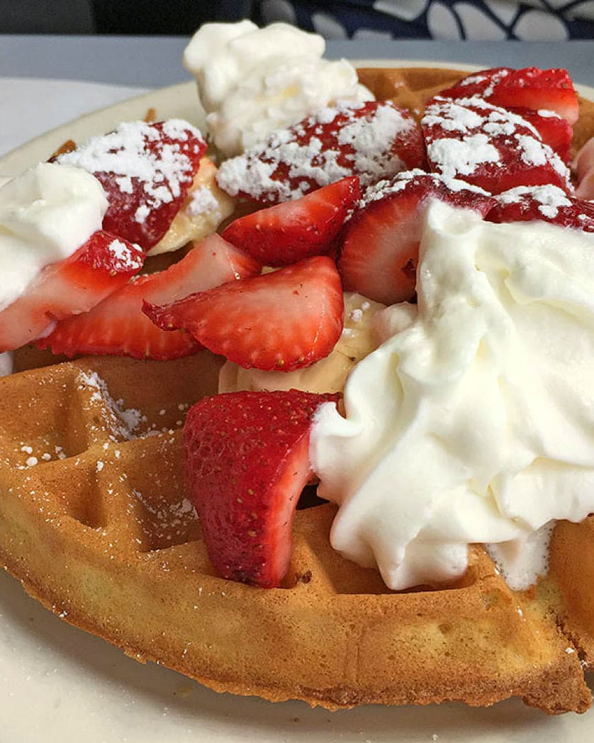 Belgian waffle piled with sliced strawberries, whipped cream, and powdered sugar